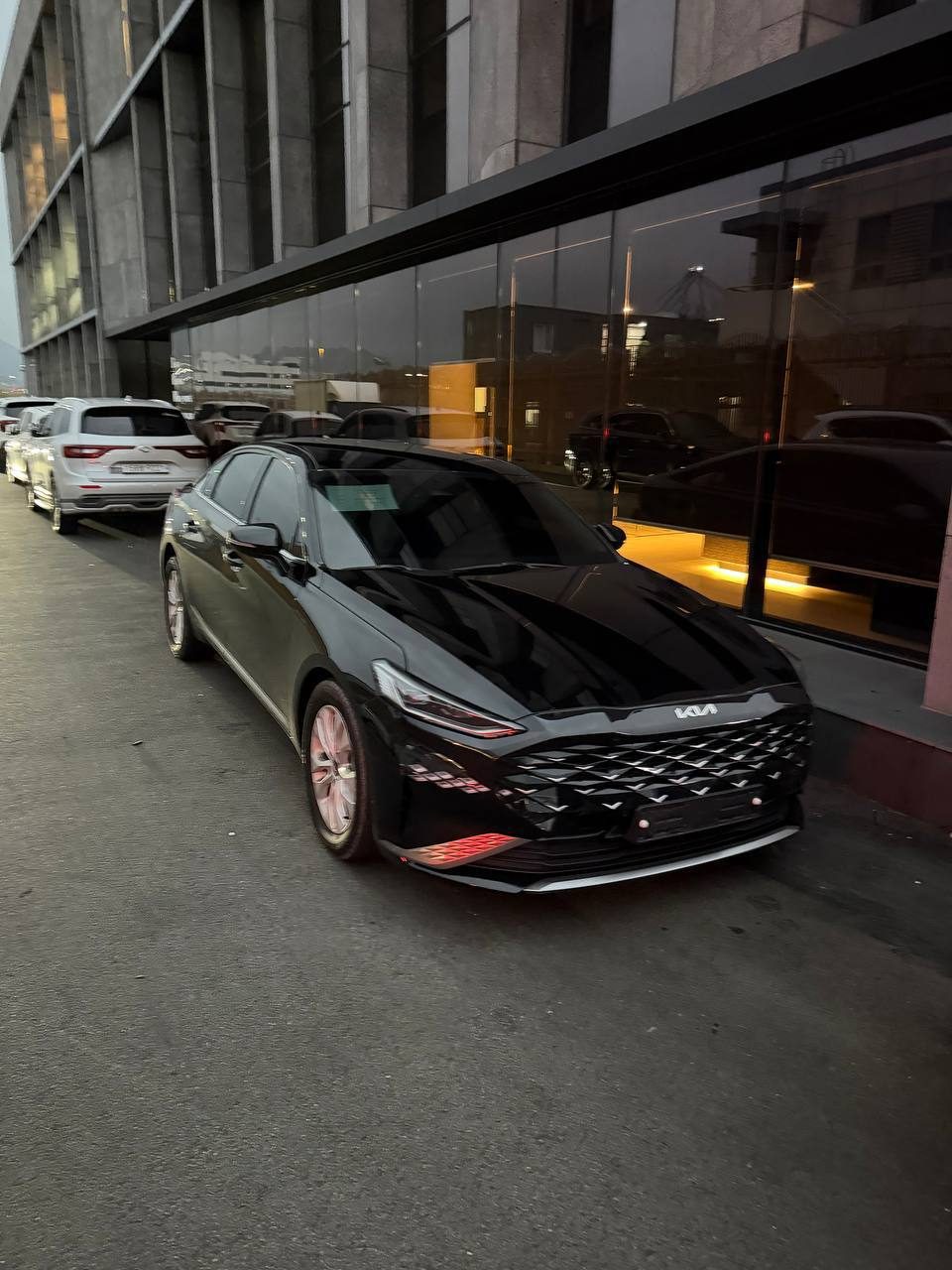 Чёрный седан Kia K8 на улице в Корее вечером